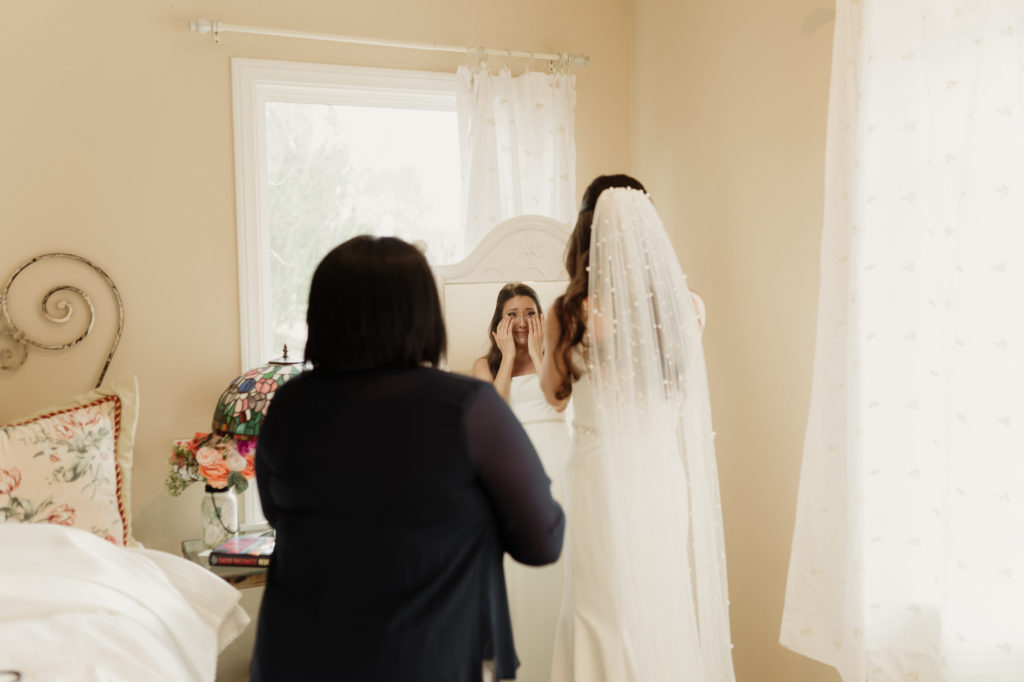 the bride and her mom look in the mirror for the first time getting ready