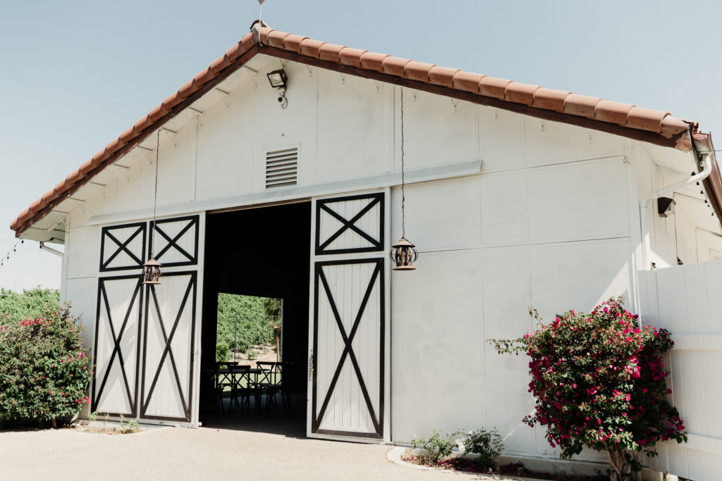a white barn with black trim and a spanish style roof at q vineyard at hummingbird nest ranch wedding venue