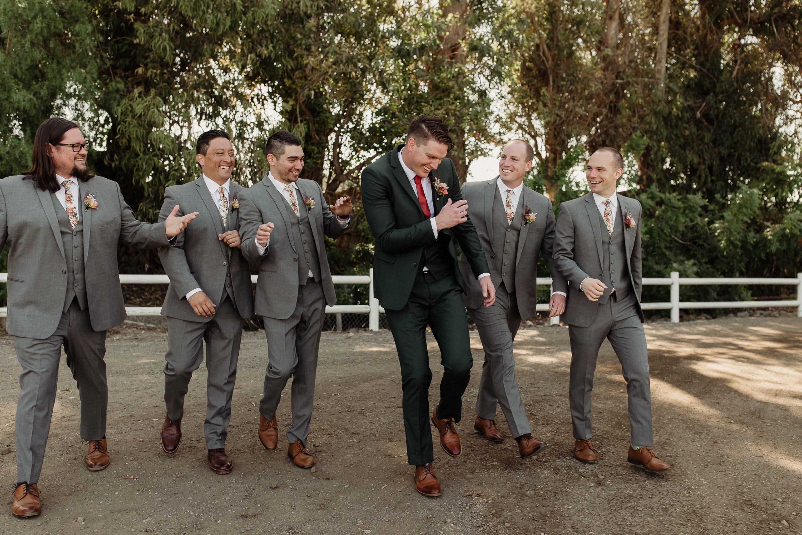 groom wearing a green suit and groomsmen wearing grey suits on a road in front tall eucalyptus trees at walnut grove weddings in moorpark