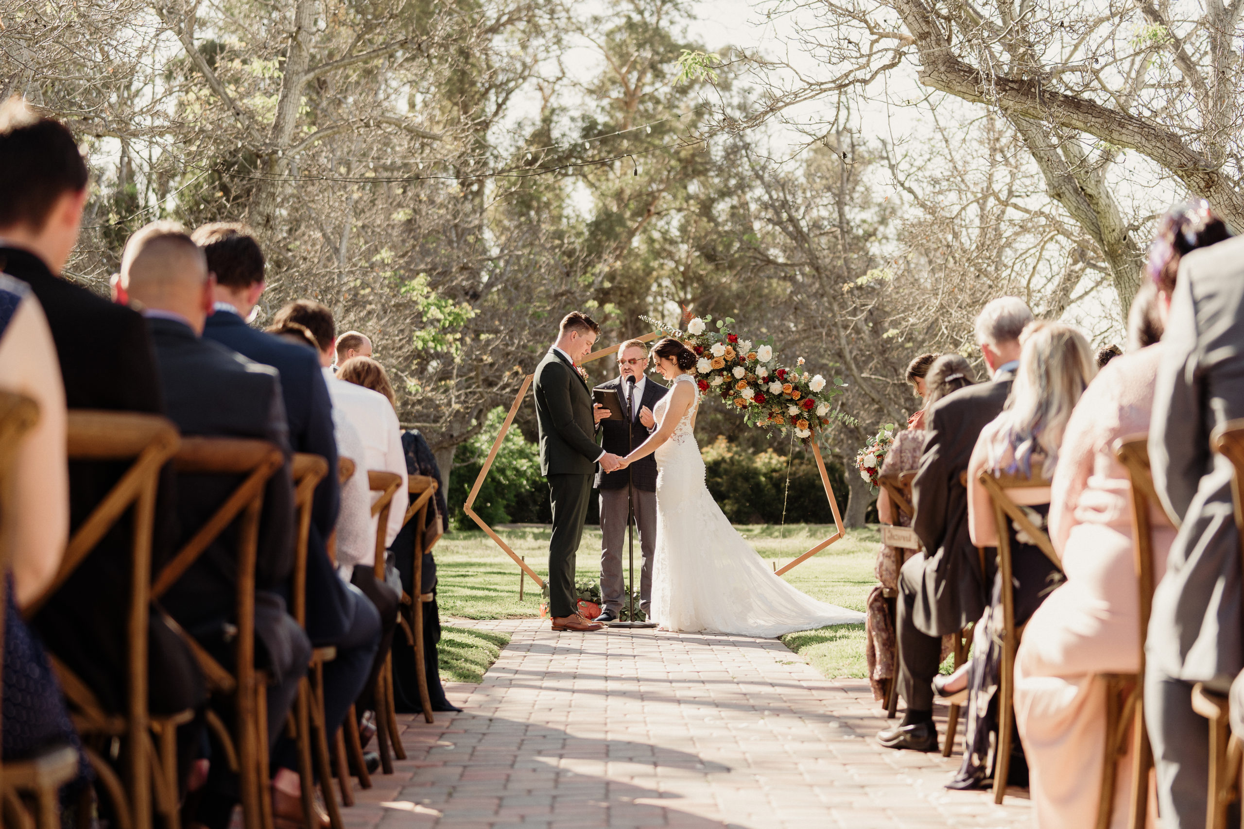 bride and groom hold hands during vows in the walnut grove in front of their arch at walnut grove weddings in moorpark