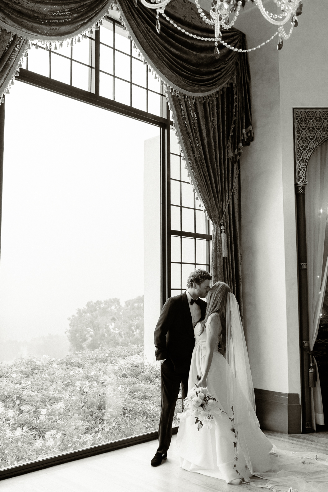 bride and groom kiss in front of floor to ceiling windows at the montecito club