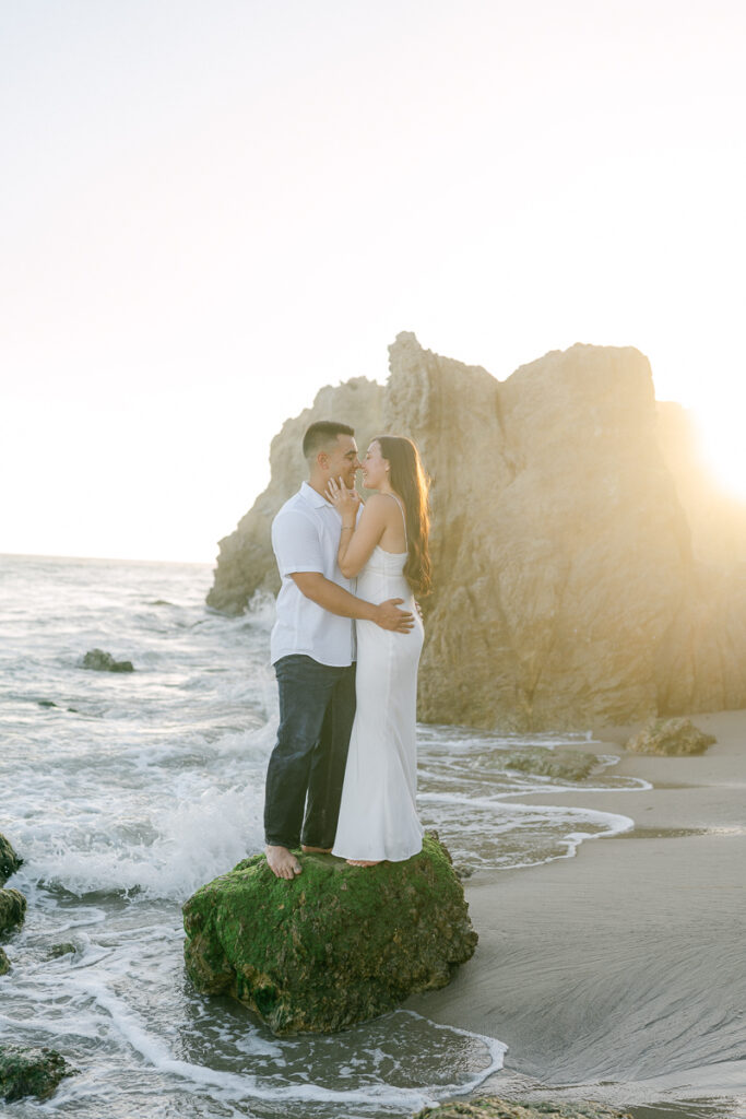 engaged couple standing on a mossy rock almost kissing at sunset at el matador beach during their engagement session captured by malibu wedding photographer magnolia west photography