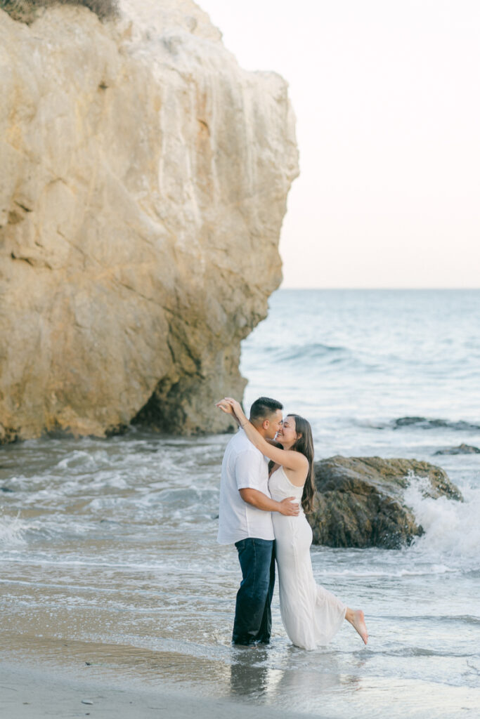 engaged couple standing in the water kissing at sunset at el matador beach during their engagement session captured by malibu wedding photographer magnolia west photography