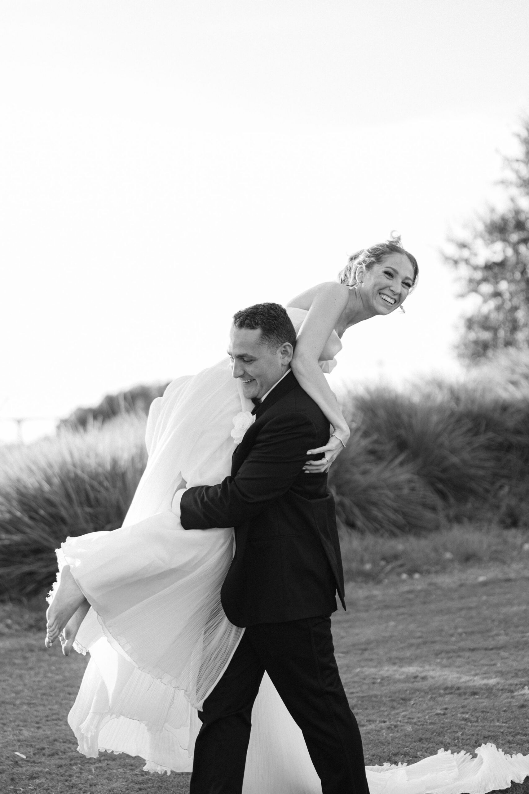 How to Choose a Wedding Photographer - Relaxed bride and groom. Black and white image of a groom with his bride thrown over his shoulder barefoot as he's running away with her.